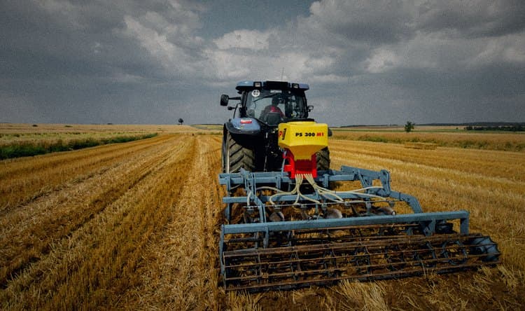 Sembradora neumática APV PS 300 M1 con tolva amarilla montada sobre cultivador, trabajando un campo de trigo bajo cielo de tormenta