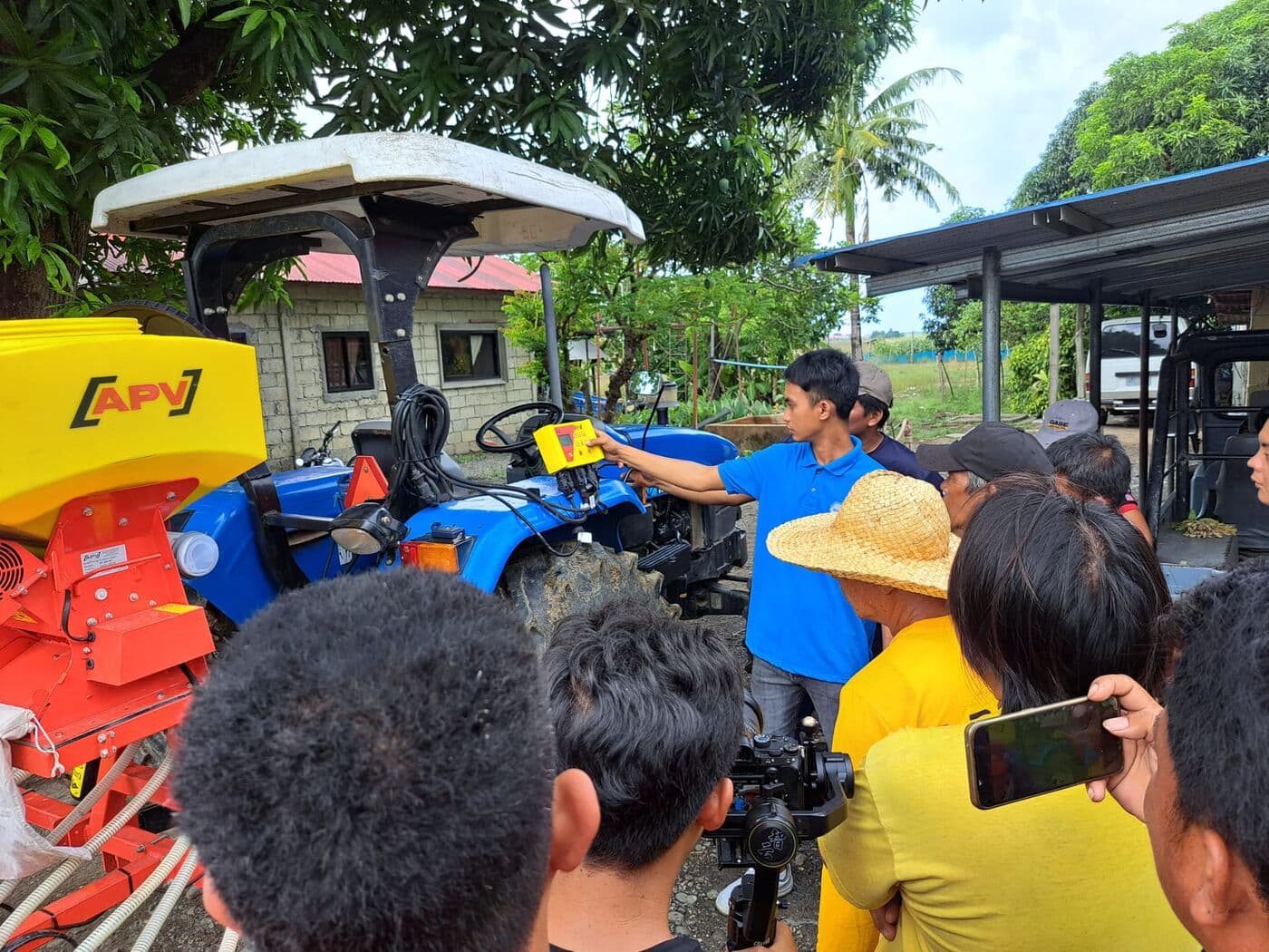 Demostración de una tolva APV montada en tractor azul, con productores alrededor tomando fotos