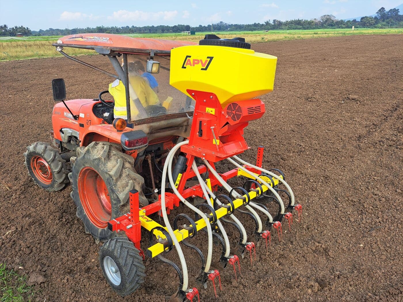 Barra sembradora con tolva APV sobre un tractor compacto rojo, en suelo preparado