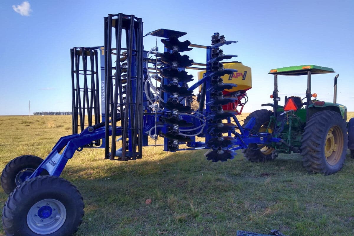 Tolva APV sobre una rastra combinada de discos y rodillo, con tractor verde