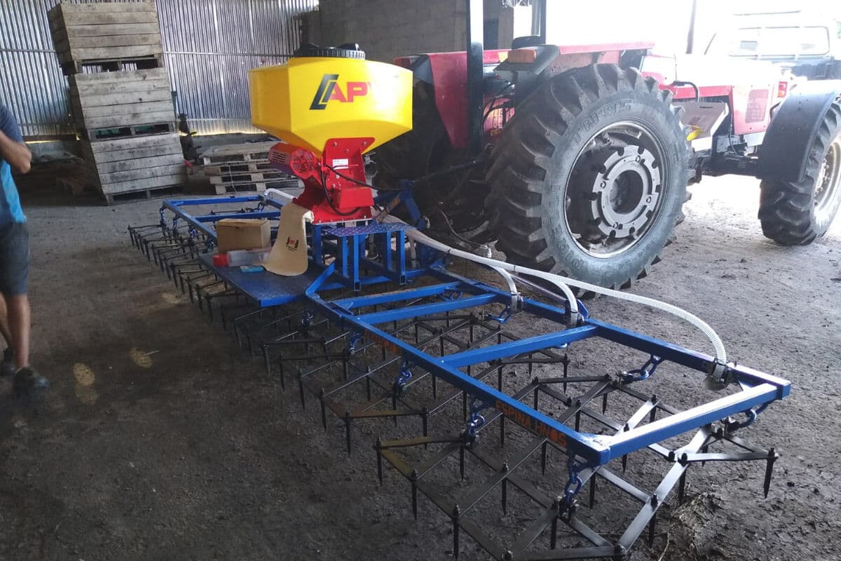 Tolva APV sobre una rastra de dientes azul, junto al tractor
