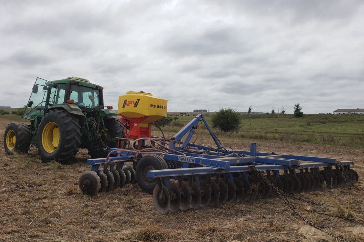 Tractor verde con rastra de discos y tolva APV trabajando el campo