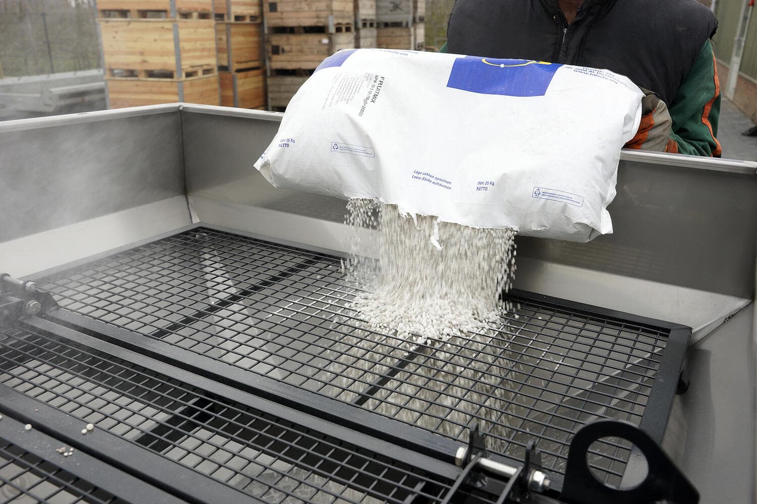 Saco de fertilizante vaciándose sobre la criba dentro de la tolva