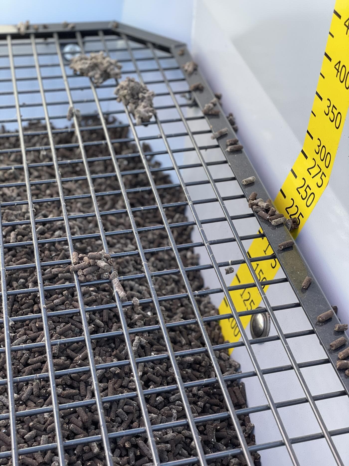 Criba de acero inoxidable con fertilizante granulado y la escala graduada amarilla de la tolva